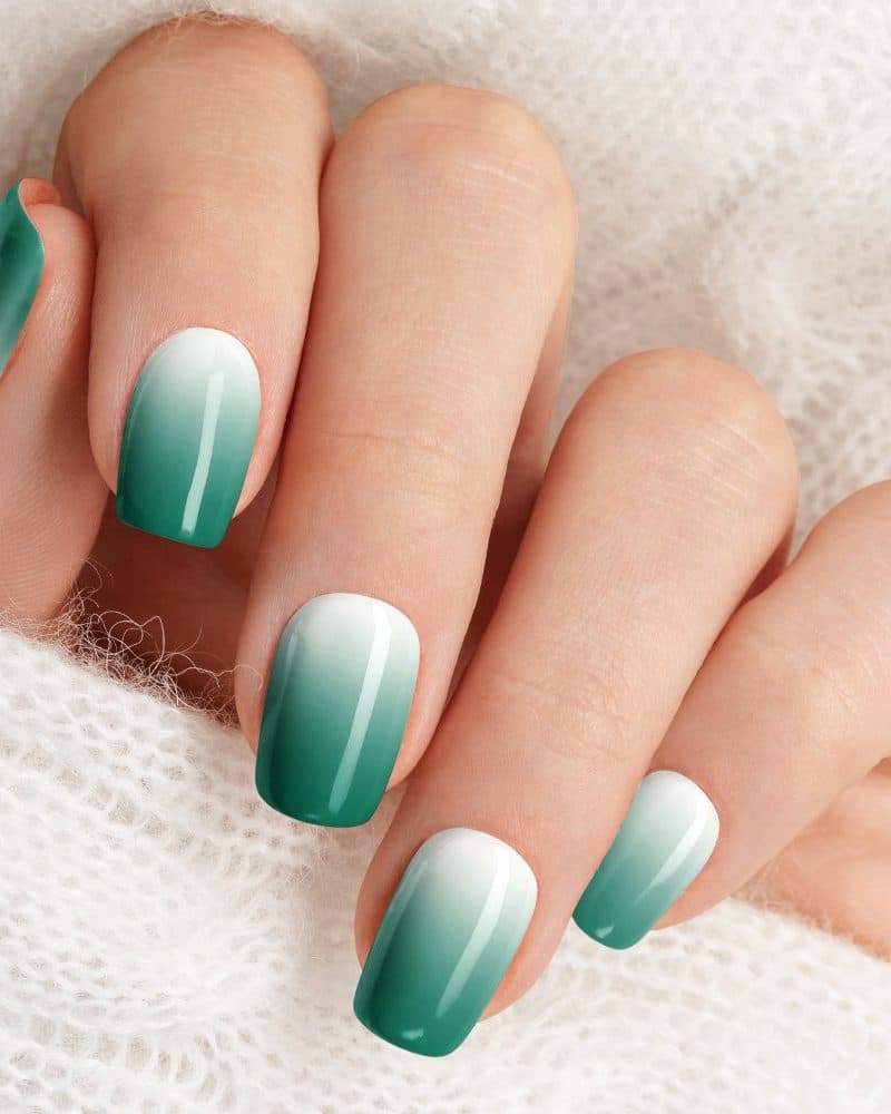 Close-up of a hand with ombre nails, transitioning from white to teal.