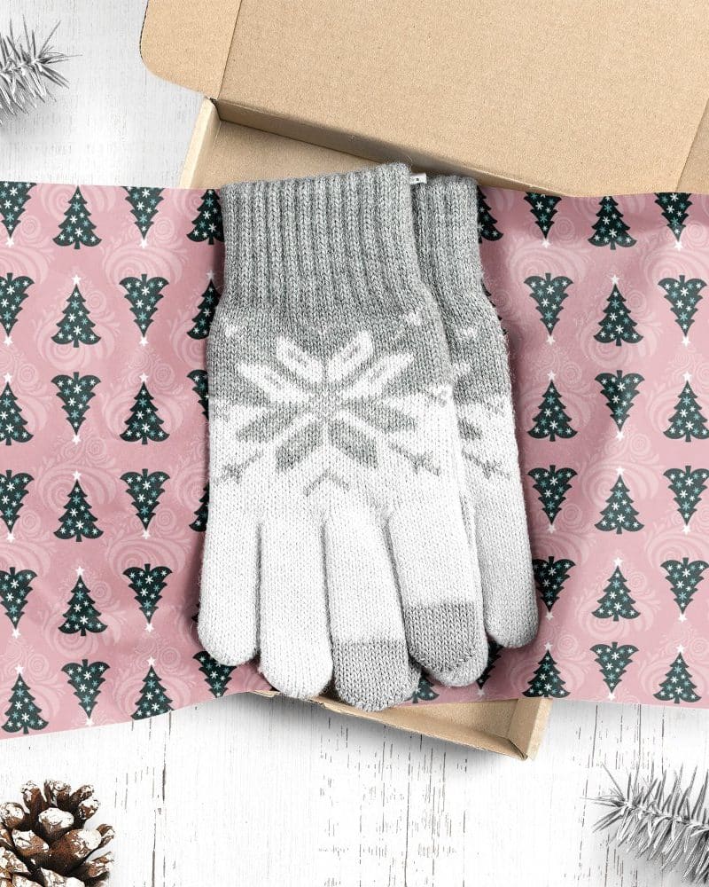 Gray and white knit gloves with snowflake pattern, in a box lined with Christmas tree wrapping paper.