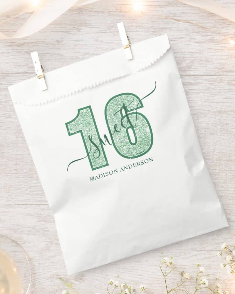 White favor bag with a green glitter design that says Sweet 16 and Madison Anderson.
