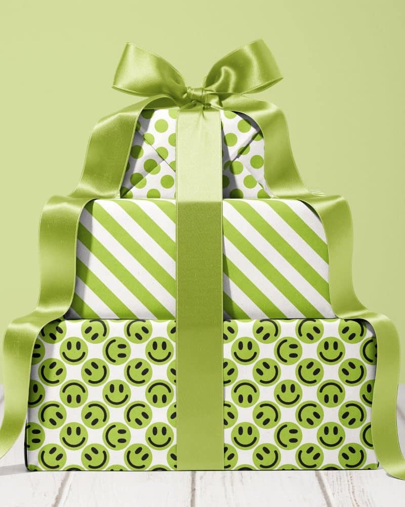 A stack of three lime green gifts, tied with a large lime green ribbon. The wrapping paper features different patterns: polka dots, stripes, and smiley faces.
