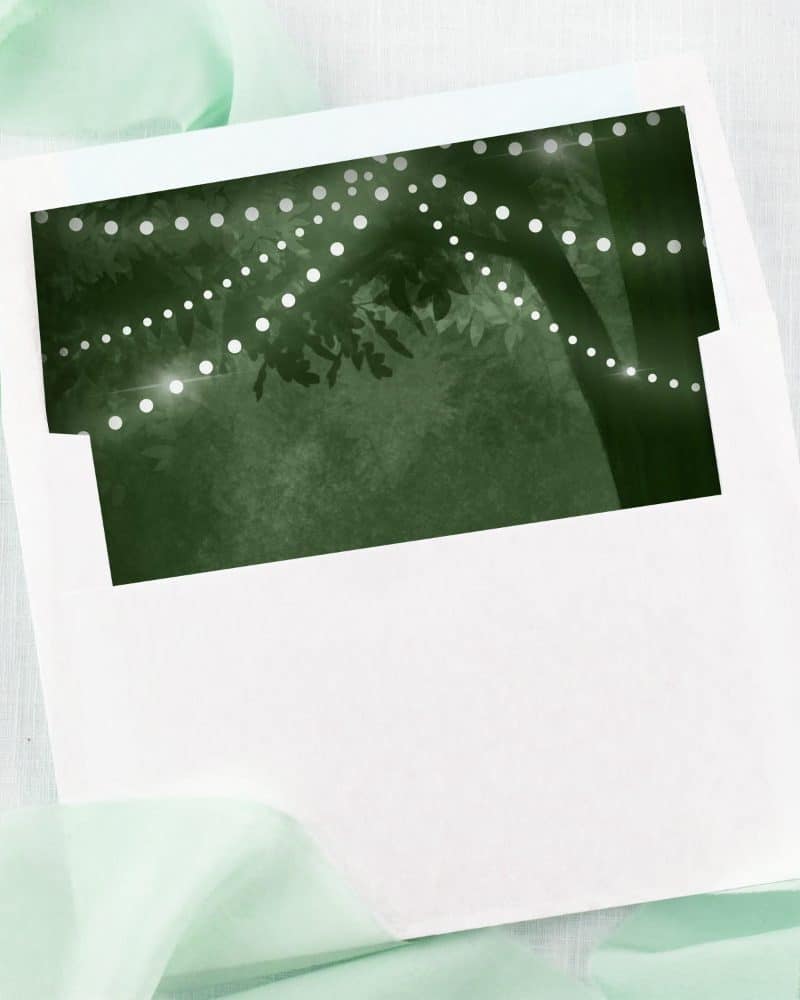 White envelope with a dark green liner featuring string lights draped on a tree.