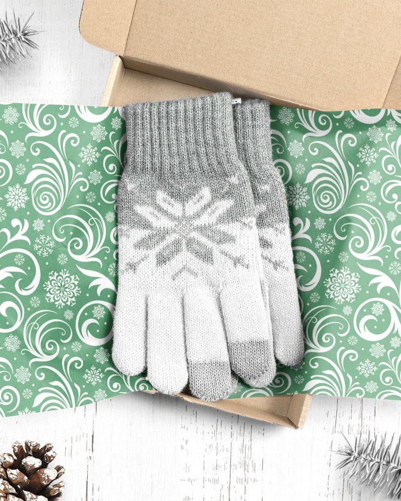 Gray and white knit gloves with snowflake pattern, presented in a gift box lined with green and white snowflake wrapping paper.