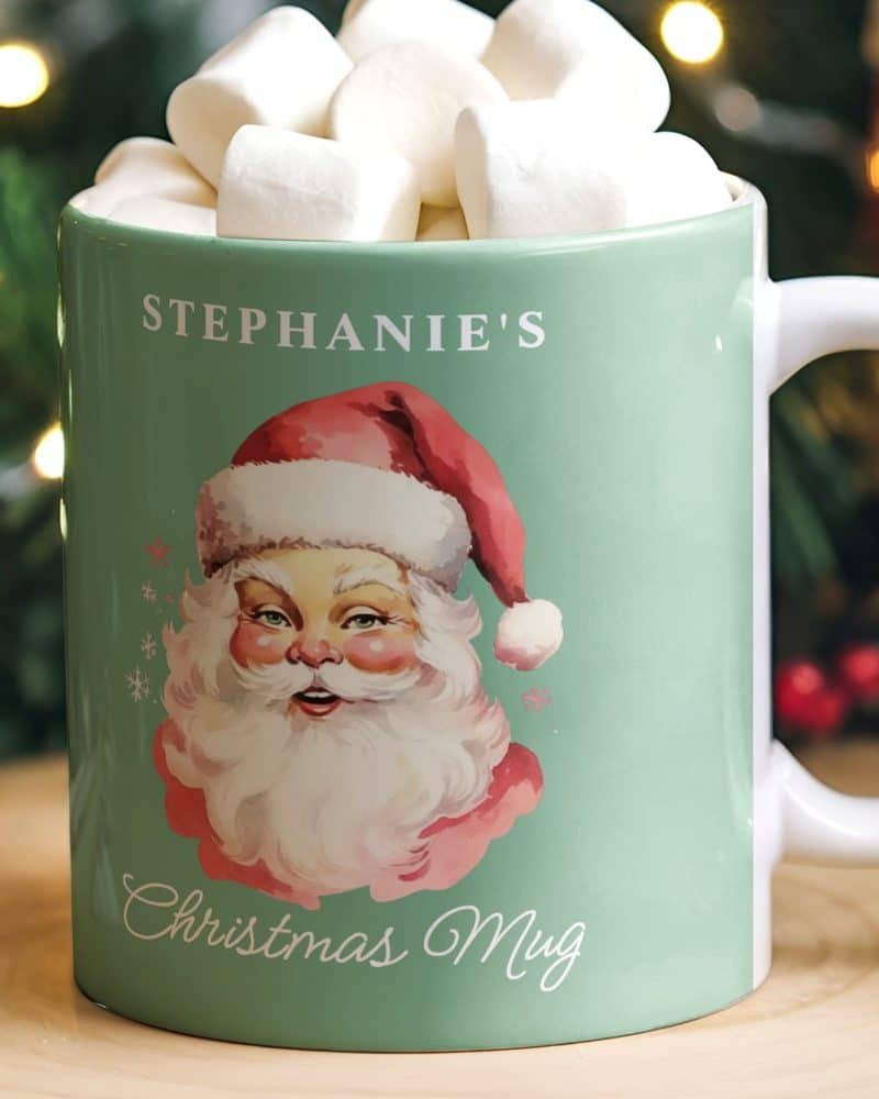 A teal Christmas mug with Stephanie's name, a vintage Santa image, and the words Christmas Mug. The mug is filled with marshmallows.