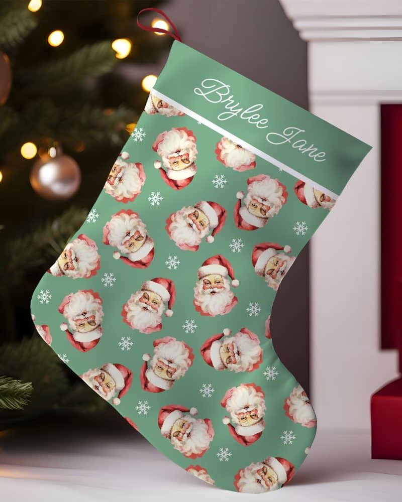 Personalized Christmas stocking with a teal background and repeating pattern of Santa Claus faces. The name Brylee Jane is printed on the cuff.