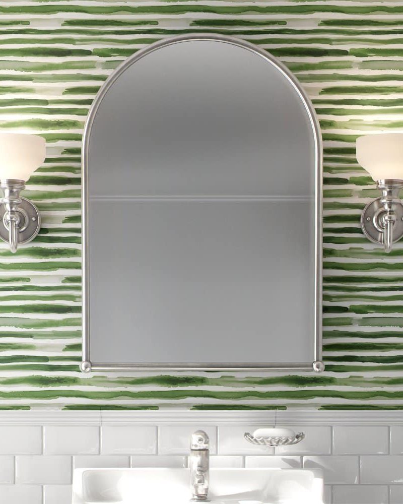 Arch-shaped mirror on a green and white striped wall above a bathroom sink.