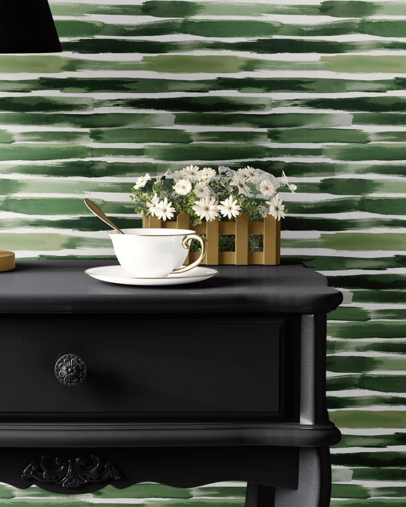 Black nightstand with a teacup and saucer, small plant, and table lamp against a green watercolor striped wall.