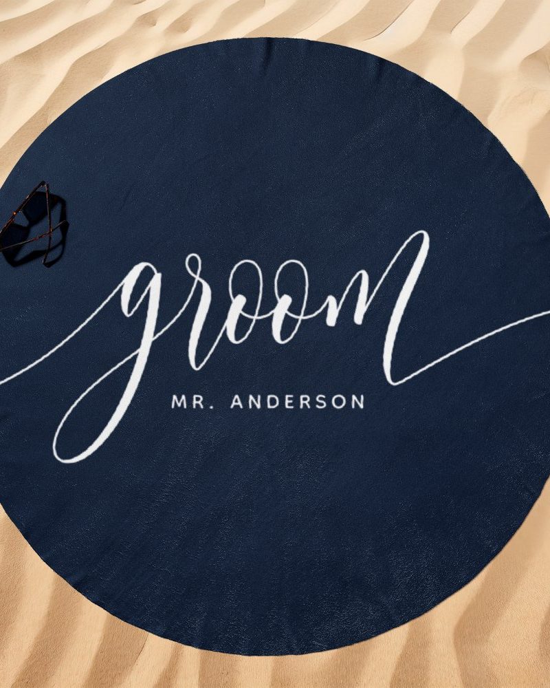 Navy blue round beach towel with the word groom in a white script font and Mr. Anderson written below.
