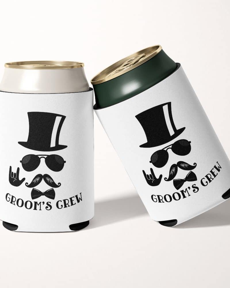 Two white can coolers featuring a black and white illustration of a man in a top hat, sunglasses, and mustache; the text Groom's Crew is printed below.