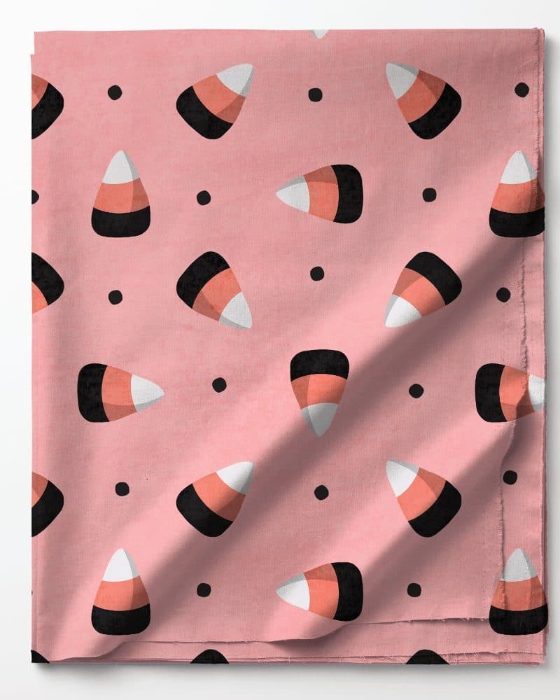 Pink fabric with a repeating pattern of candy corn and small black dots.