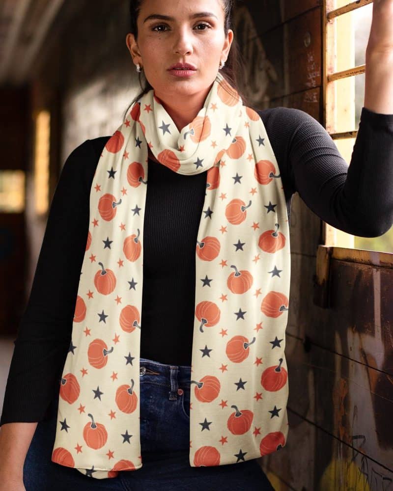 Woman wearing a cream-colored scarf with orange pumpkins and black stars.