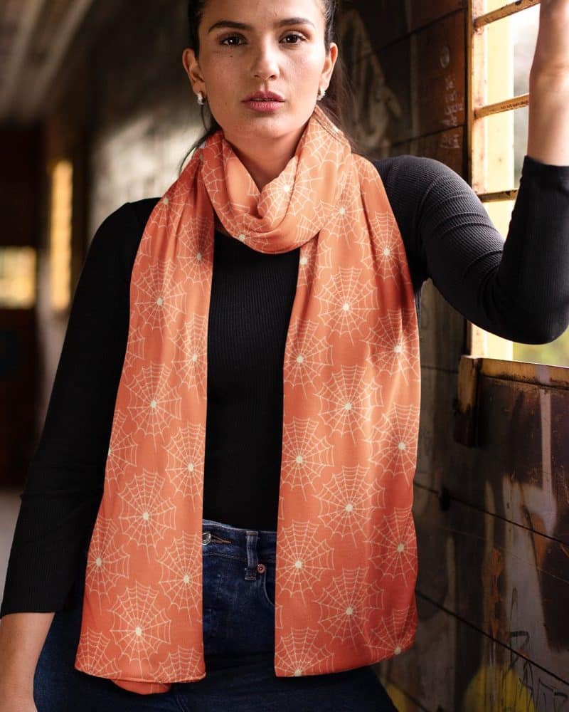 Woman wearing an orange scarf with a spiderweb pattern.