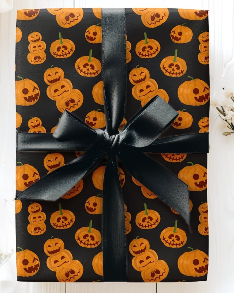 A gift wrapped in black Halloween-themed wrapping paper featuring orange jack-o'-lantern faces, tied with a black ribbon.