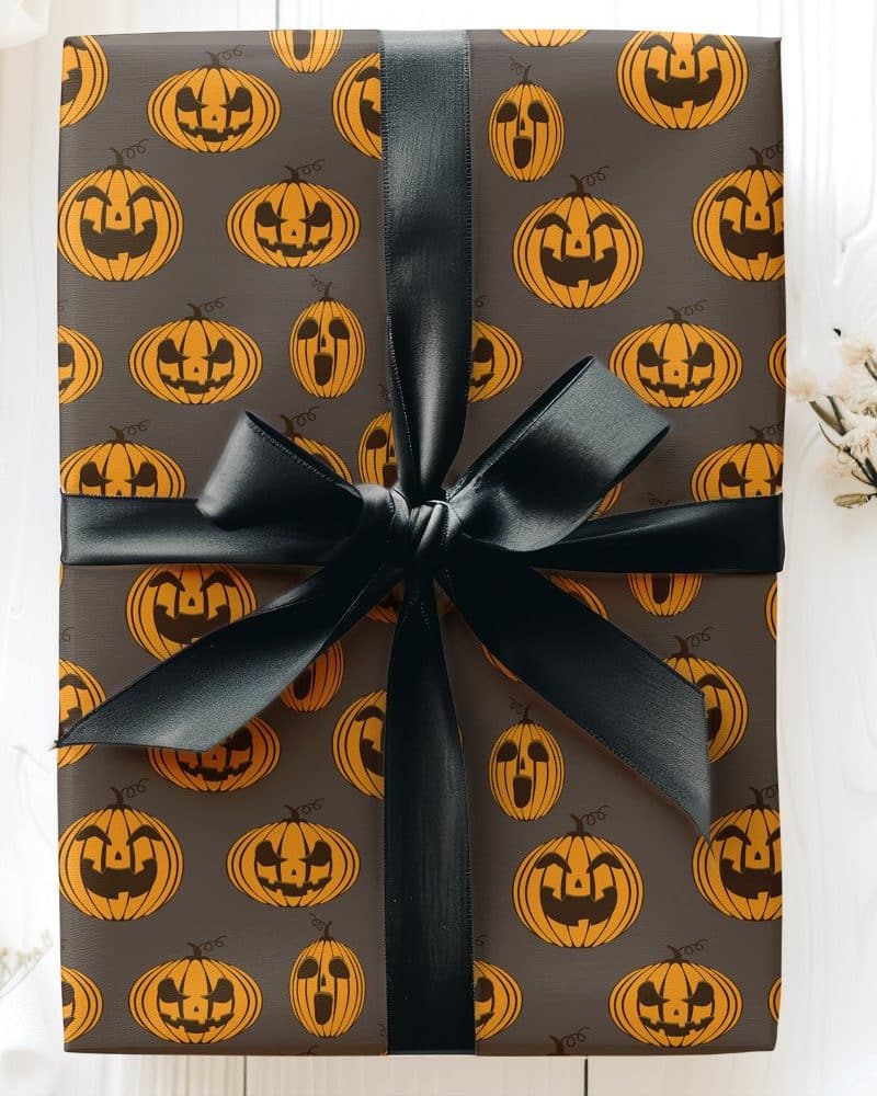 Halloween gift wrapped in dark gray paper with a repeating pattern of orange jack-o'-lanterns and tied with a black ribbon.