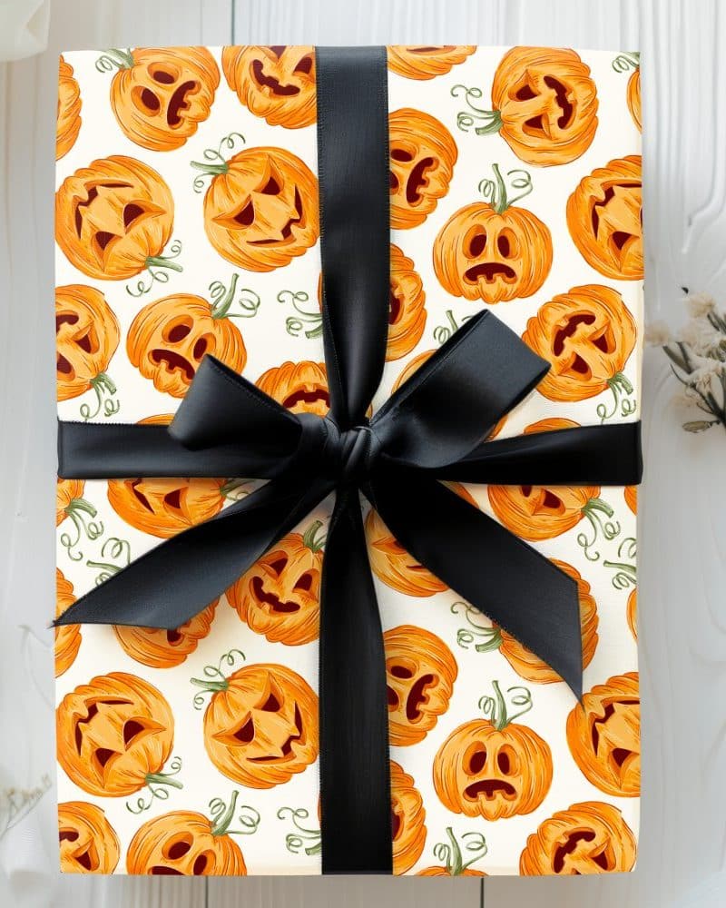 Gift wrapped in Halloween-themed wrapping paper featuring a pattern of carved pumpkins and tied with a black ribbon.