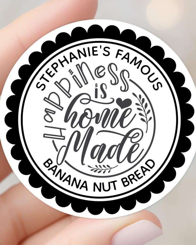 A round sticker with black scalloped edging and white background featuring the text: Stephanie's Famous Happiness is Homemade Banana Nut Bread.