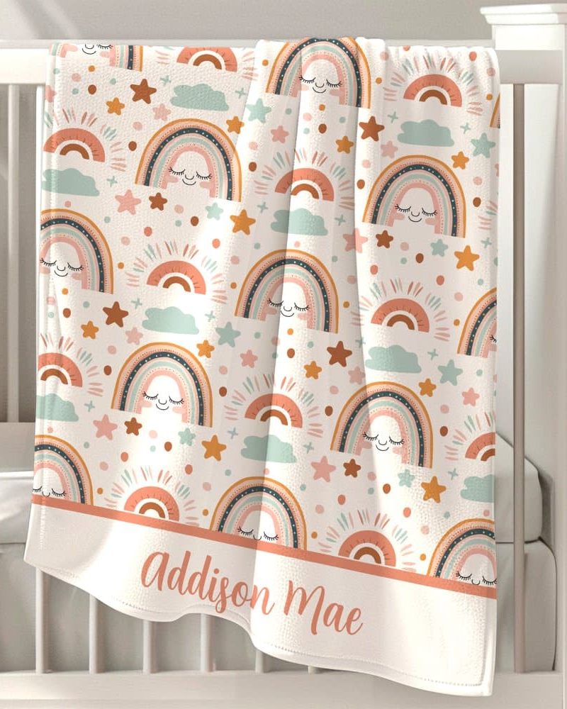 Personalized baby blanket with a pattern of pastel rainbows, stars, and clouds. The name Addison Mae is embroidered at the bottom.