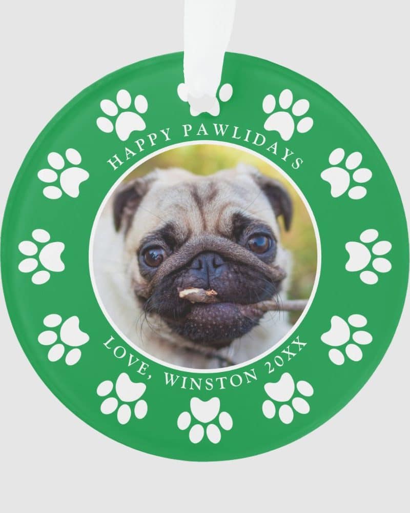 Green circular ornament featuring a pug dog in a central photo surrounded by paw prints. The text reads Happy Pawlidays and Love, Winston 20XX.