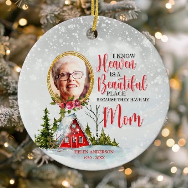 Round Christmas Ornament With A Photo Of A Woman, Text Reading I Know Heaven Is A Beautiful Place Because They Have My Mom, And A Winter Scene With A Small House. The Woman'S Name And Birth And Death Years Are Also Included.