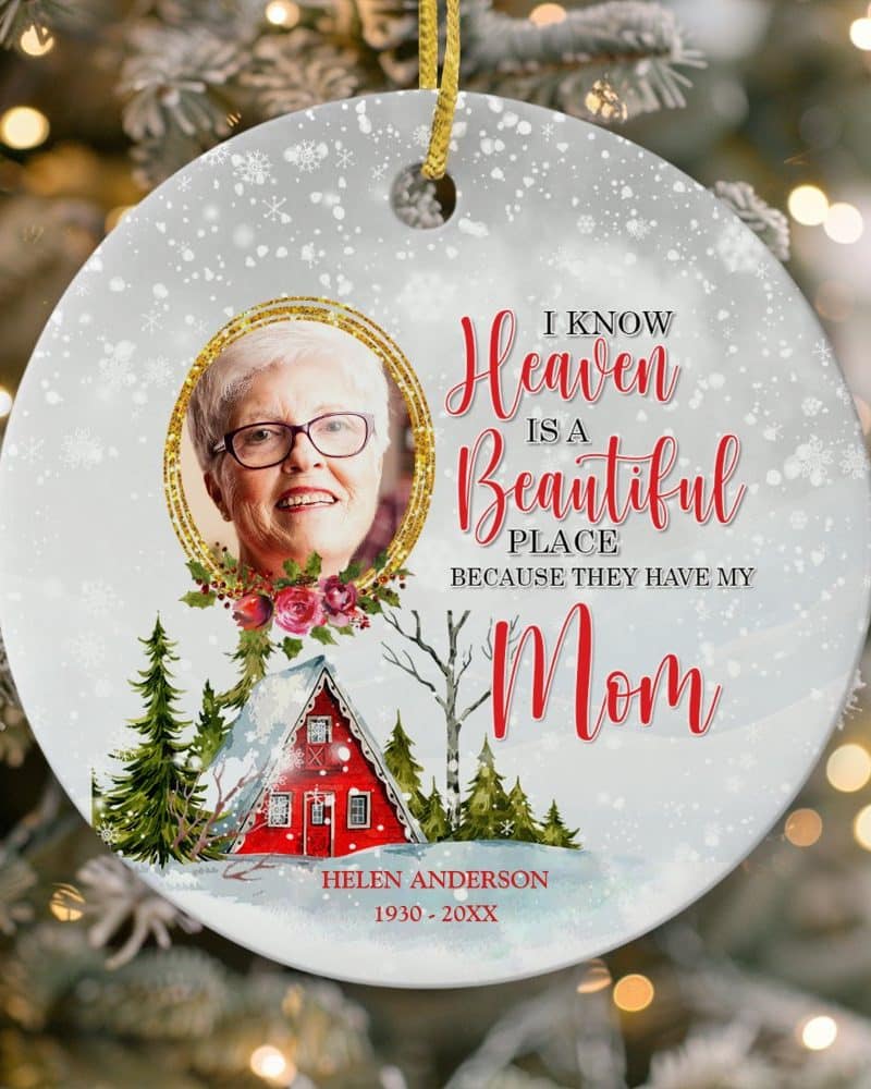 Round Christmas ornament with a photo of a woman, text reading I know Heaven is a Beautiful Place because they have my Mom, and a winter scene with a small house. The woman's name and birth and death years are also included.