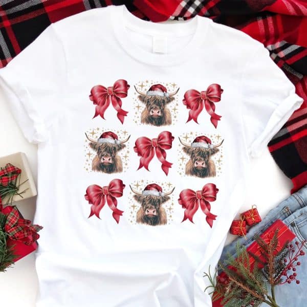 White T-Shirt With A Repeating Pattern Of Highland Cows Wearing Santa Hats And Red Bows.
