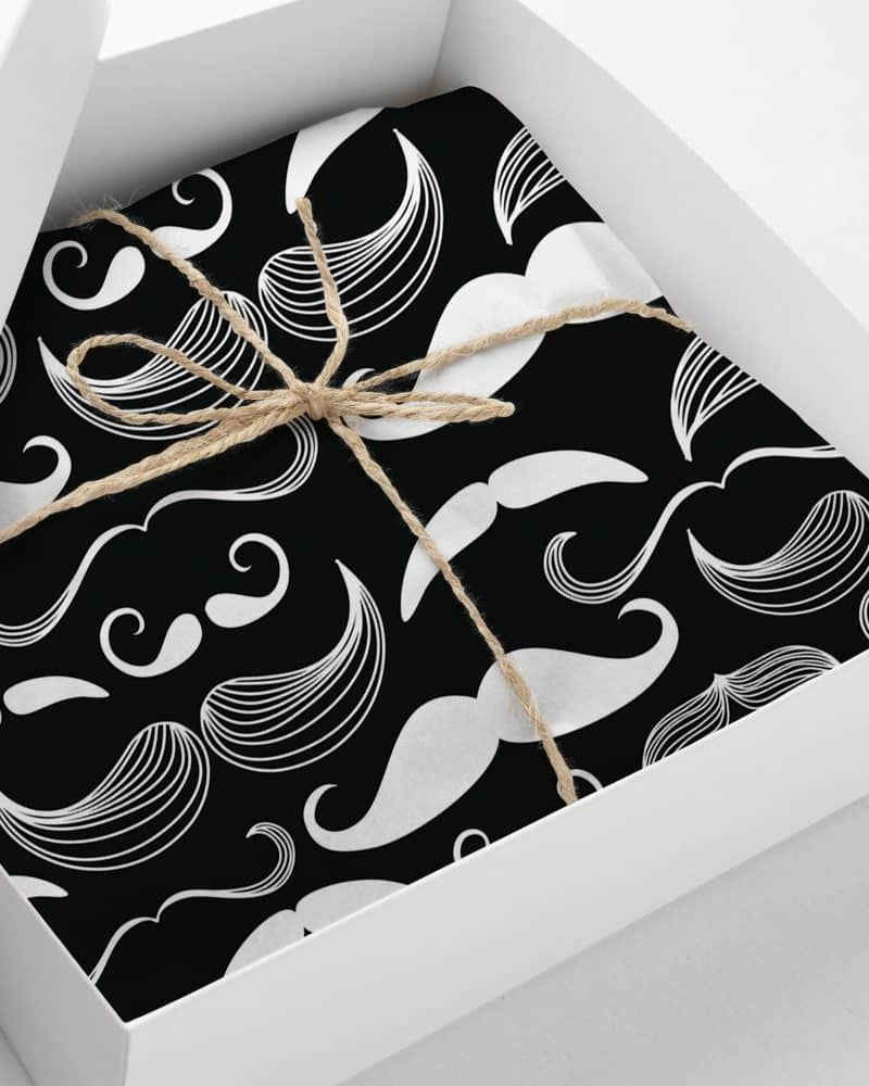 A gift box containing a black and white present wrapped in paper with a repeating pattern of mustaches. The package is tied with twine.