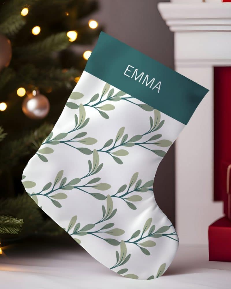 Personalized Christmas stocking with a teal cuff and a white body featuring a repeating leaf pattern. The name Emma is on the cuff.