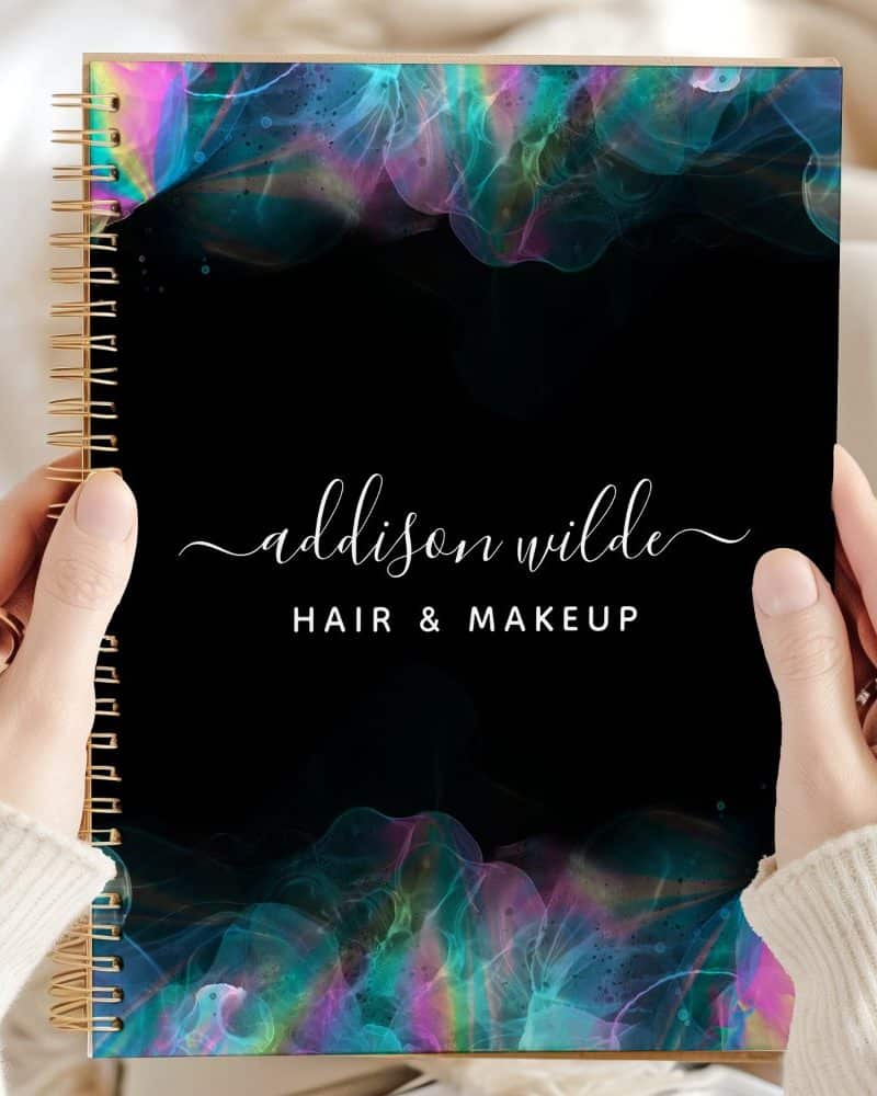 Spiral-bound notebook with a black cover featuring iridescent teal and purple abstract designs and the name Addison Wilde Hair & Makeup.