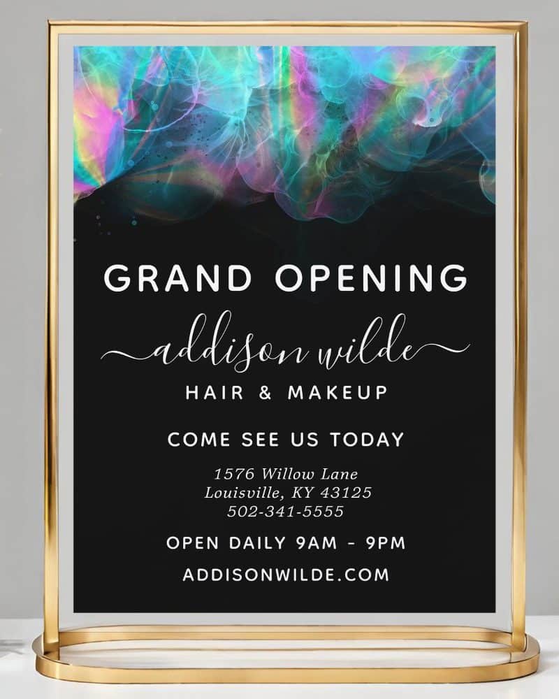 Gold-framed sign announcing the grand opening of Addison Wilde Hair & Makeup, featuring a colorful abstract design.
