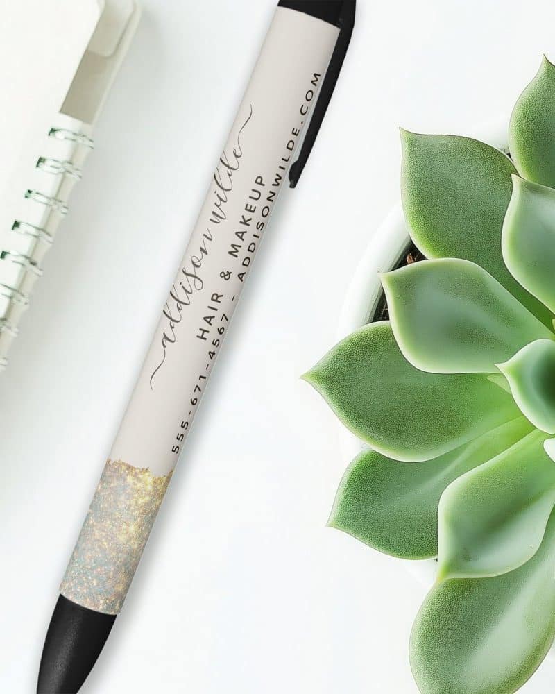 A pen with gold glitter and the name Addison Wilde, hair and makeup artist, and contact information printed on it.