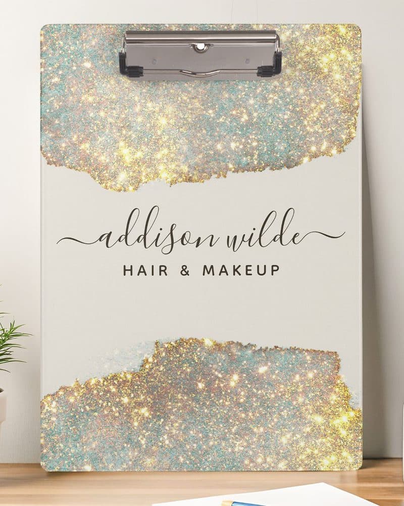 A clipboard with a sparkly gold and teal design, the name Addison Wilde Hair & Makeup.