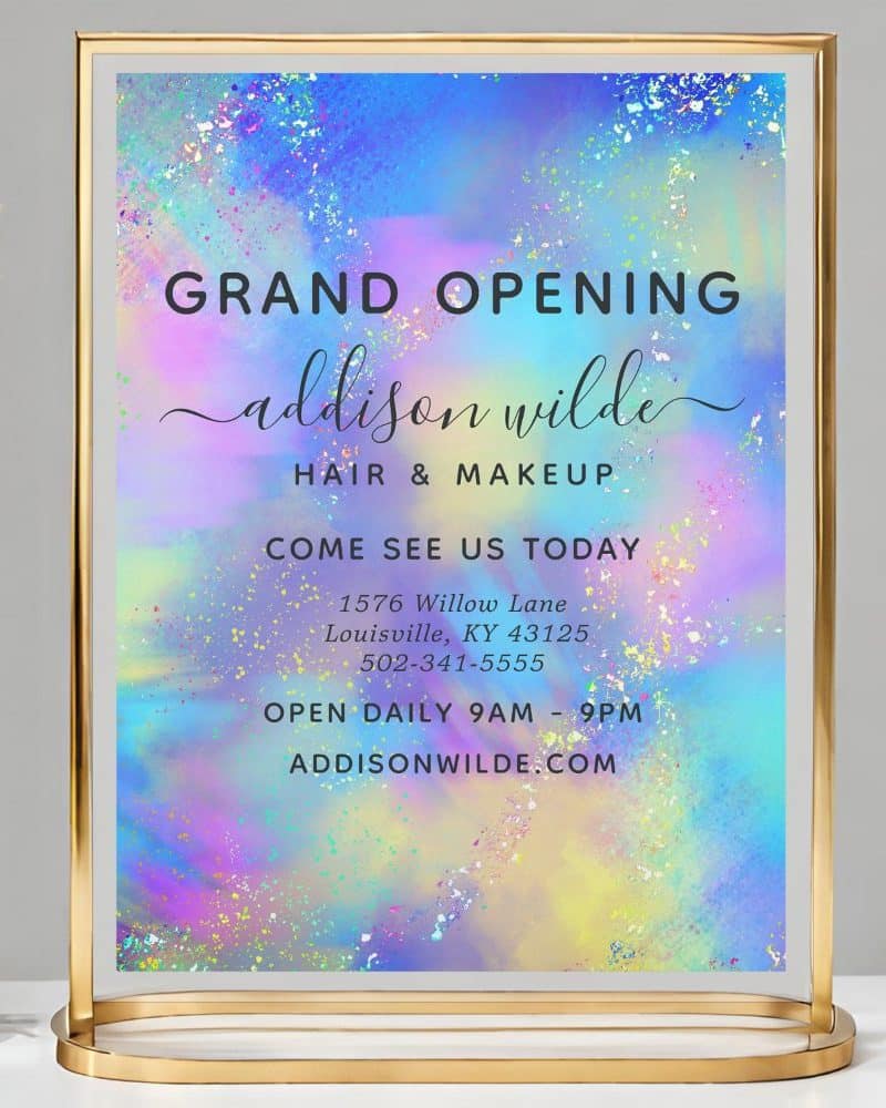 A pastel-colored grand opening sign for Addison Wilde Hair & Makeup, displaying the business's address, phone number, and website.