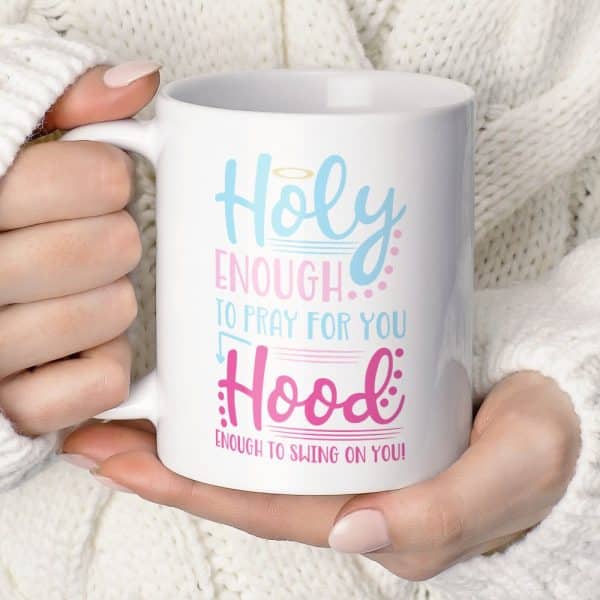 A Hand Holds A White Coffee Mug With Light Blue And Pink Text That Reads Holy Enough To Pray For You Hood Enough To Swing On You.