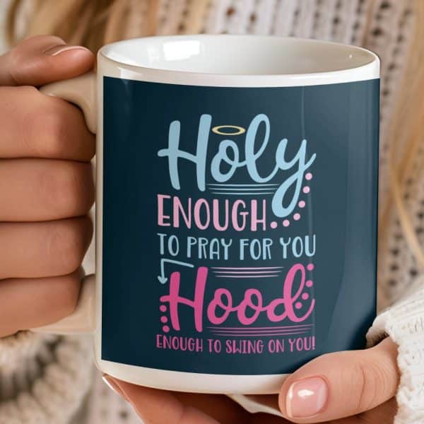 A White Coffee Mug With A Dark Blue Design That Says Holy Enough To Pray For You, Hood Enough To Swing On You.