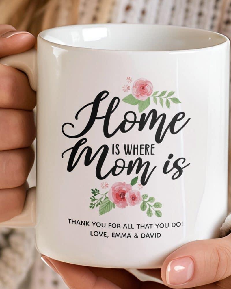 White coffee mug with the text Home is where Mom is, surrounded by pink flowers.