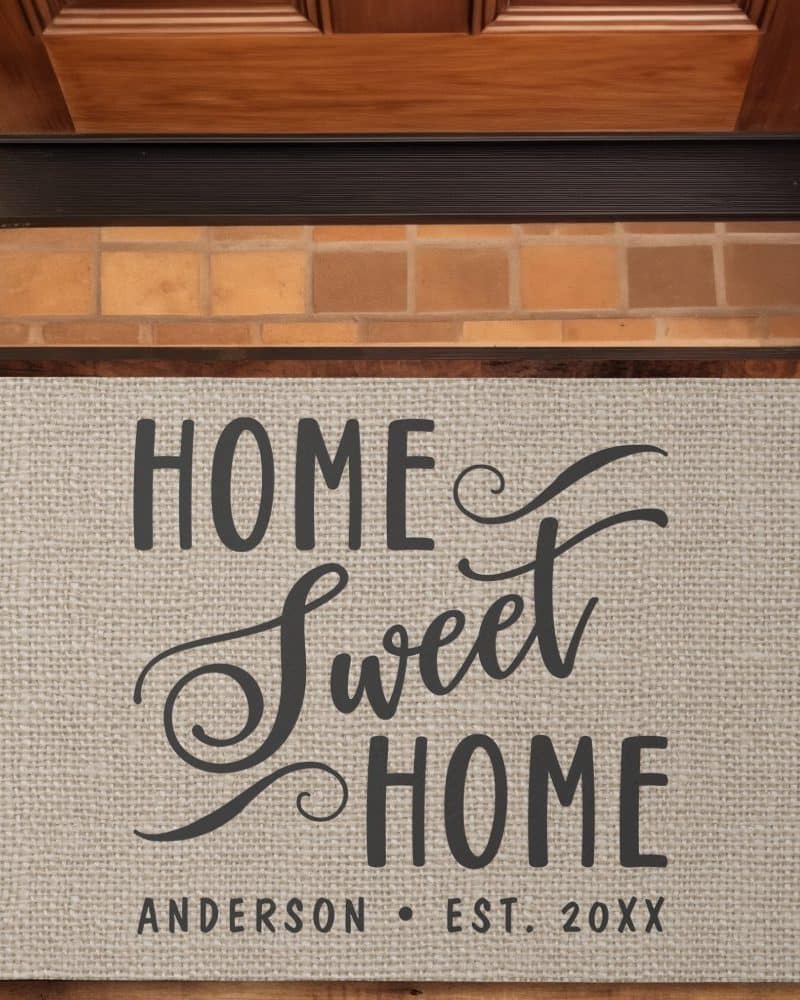 Beige doormat with the text Home Sweet Home in a stylized font, and the family name Anderson and established year below.