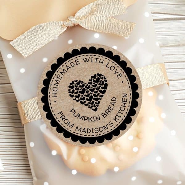 A Round Label With A Black Border And A Kraft Paper Background Shows A Heart Made Of Smaller Hearts. The Text Reads Homemade With Love, Pumpkin Bread, From Madisons Kitchen. The Label Is Attached To A Cellophane Bag Of Baked Goods.
