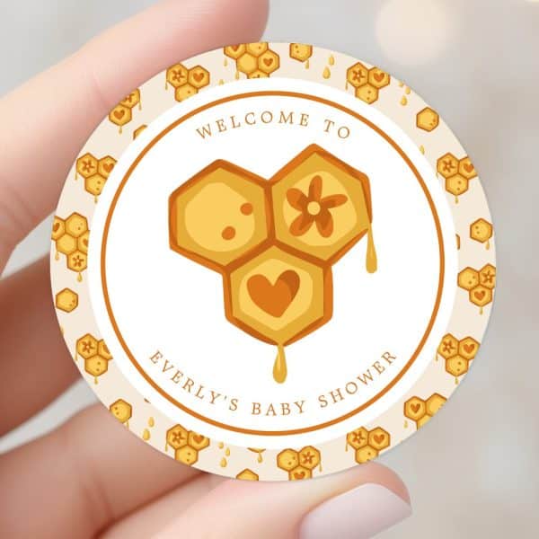A Round Baby Shower Invitation Featuring A Honeycomb Design With A Heart And Flower. The Text Says Welcome To Everly'S Baby Shower.