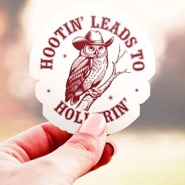 A Hand Holds Up A Sticker Featuring A Cowboy Hat-Wearing Owl Perched On A Branch. The Text Around The Owl Reads Hootin Leads To Hollerin.