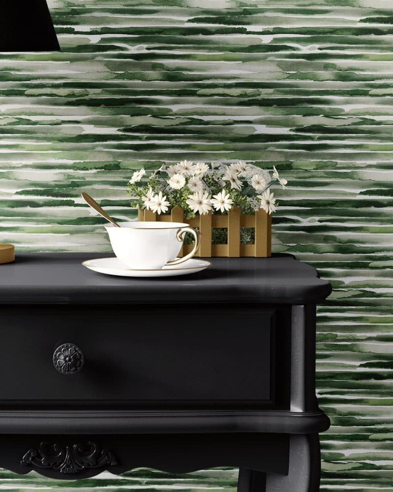 A teacup and saucer sit on a dark wooden side table, in front of a wall with green watercolor stripes.
