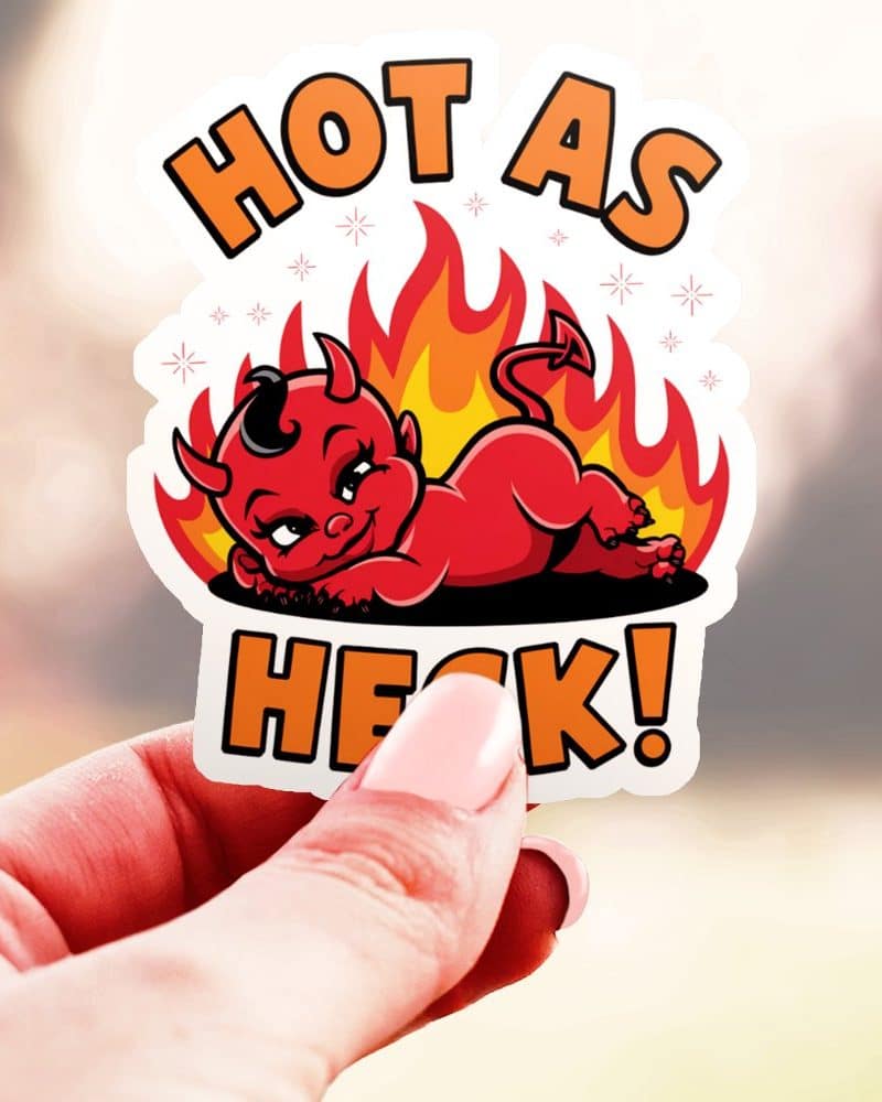 Hand holding a sticker of a devil baby surrounded by flames, with the text Hot as Heck.