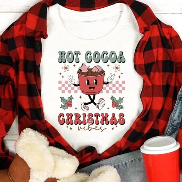 White Shirt With A Cartoon Hot Cocoa Cup Graphic And The Text Hot Cocoa Christmas Vibes.