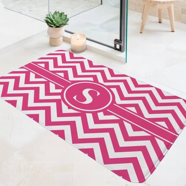 Pink And White Chevron Patterned Bath Mat With A Pink Circle Monogram In The Center.