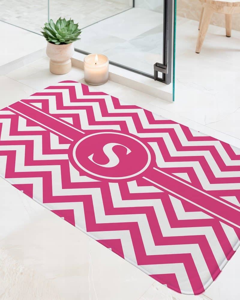 Pink and white chevron patterned bath mat with a pink circle monogram in the center.