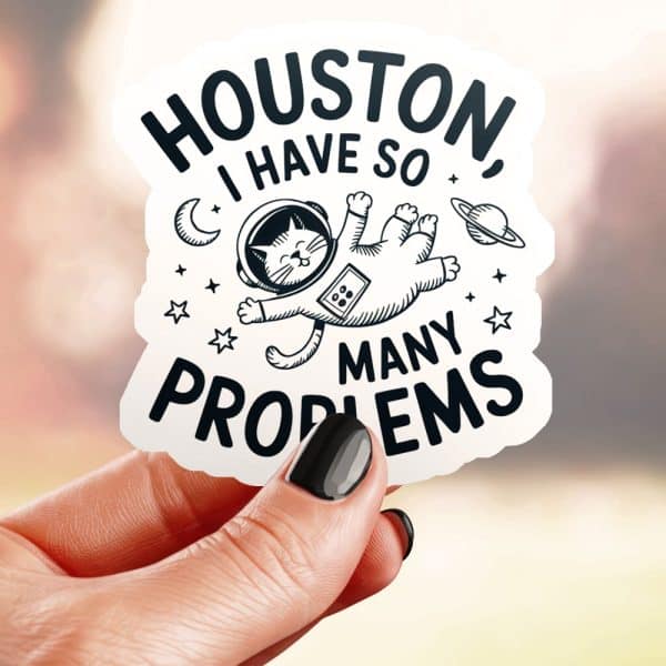 A Hand Holds A Sticker Featuring A Cat In An Astronaut Suit Floating In Space, With The Text Houston, I Have So Many Problems.