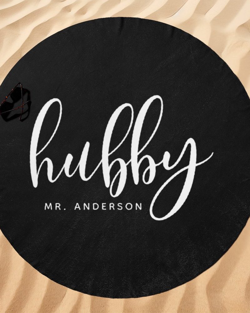 Black round beach towel with the word hubby in white cursive lettering and Mr. Anderson below it.