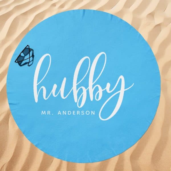 Light Blue Round Beach Towel With The Word Hubby In White Script Lettering And Mr. Anderson Below It. A Pair Of Sunglasses Rests On The Towel.