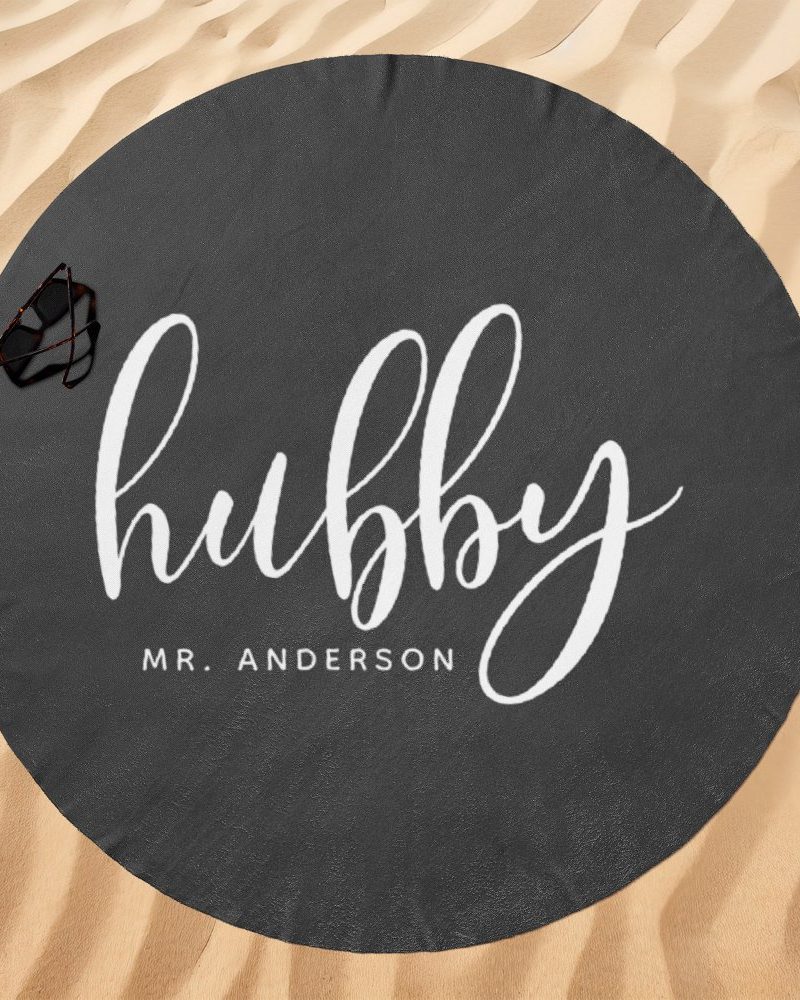 Dark gray round beach towel with the word hubby in white script and Mr. Anderson below it.
