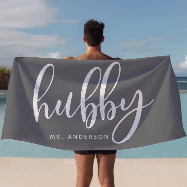 A Man Holds A Gray Beach Towel Behind Him. The Towel Says Hubby In Stylized White Lettering, With Mr. Anderson Below.