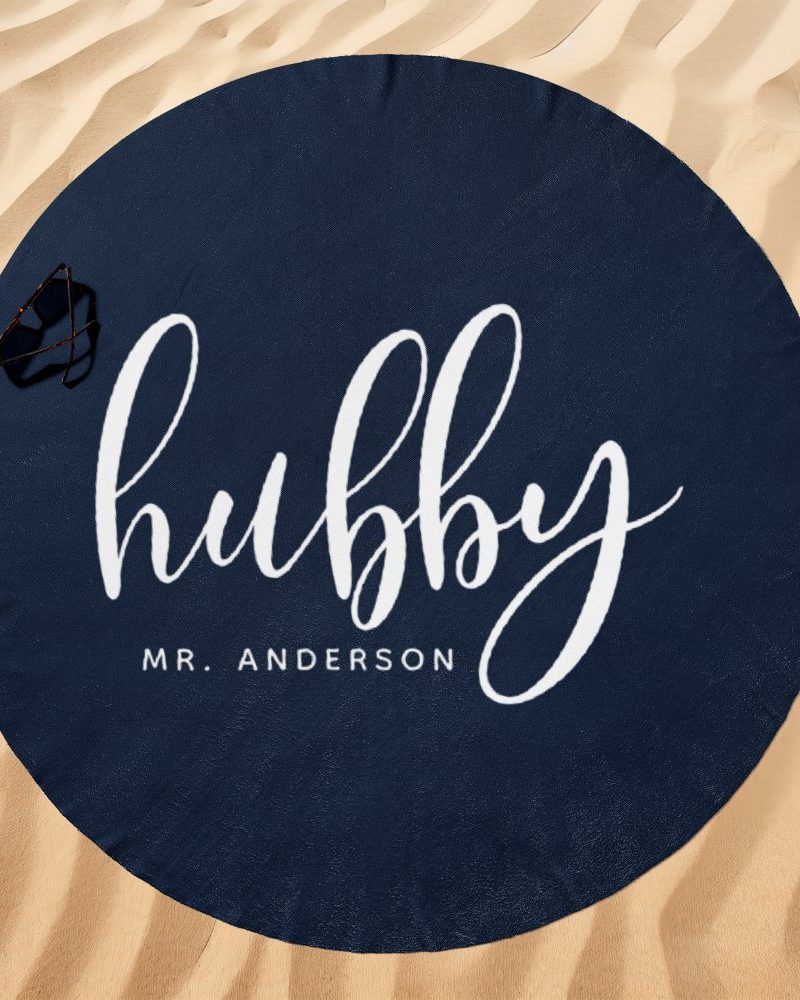 Navy blue round beach towel with the word hubby in white script lettering and Mr. Anderson below it.