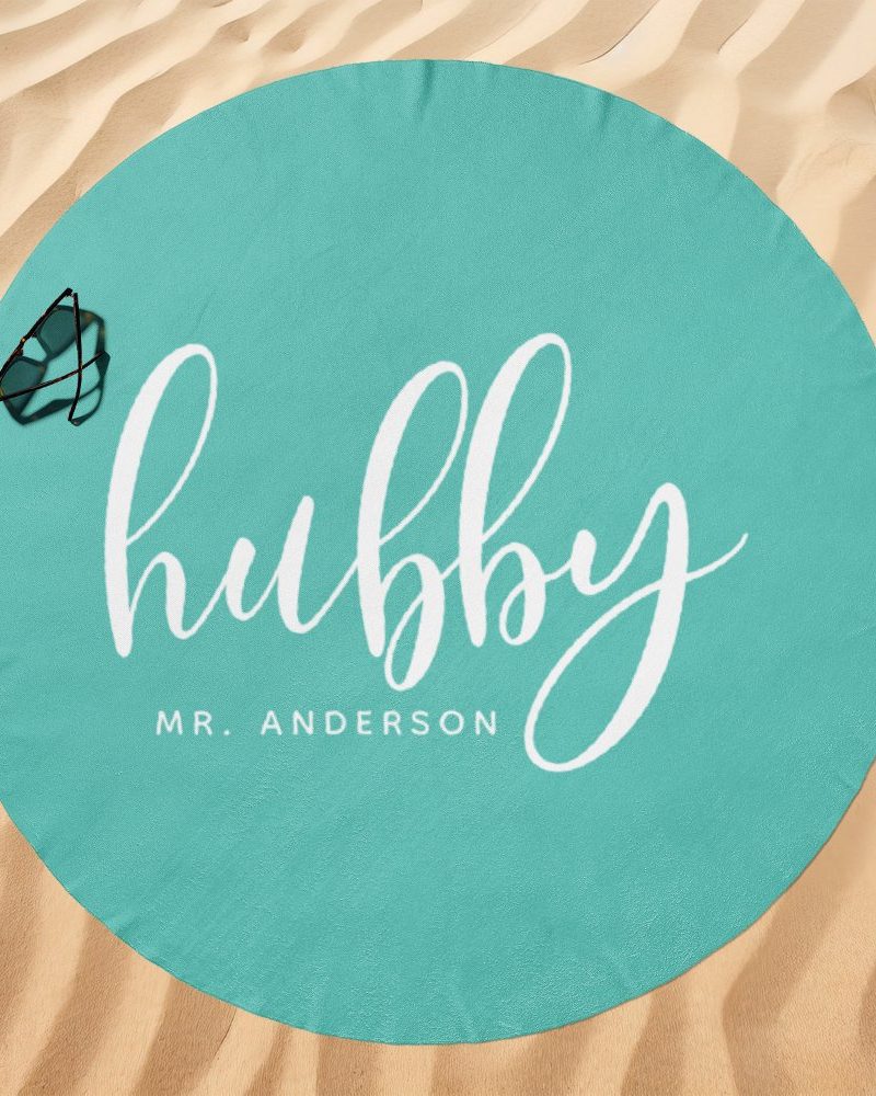 Teal round beach towel with the word hubby in white cursive lettering and Mr. Anderson below.